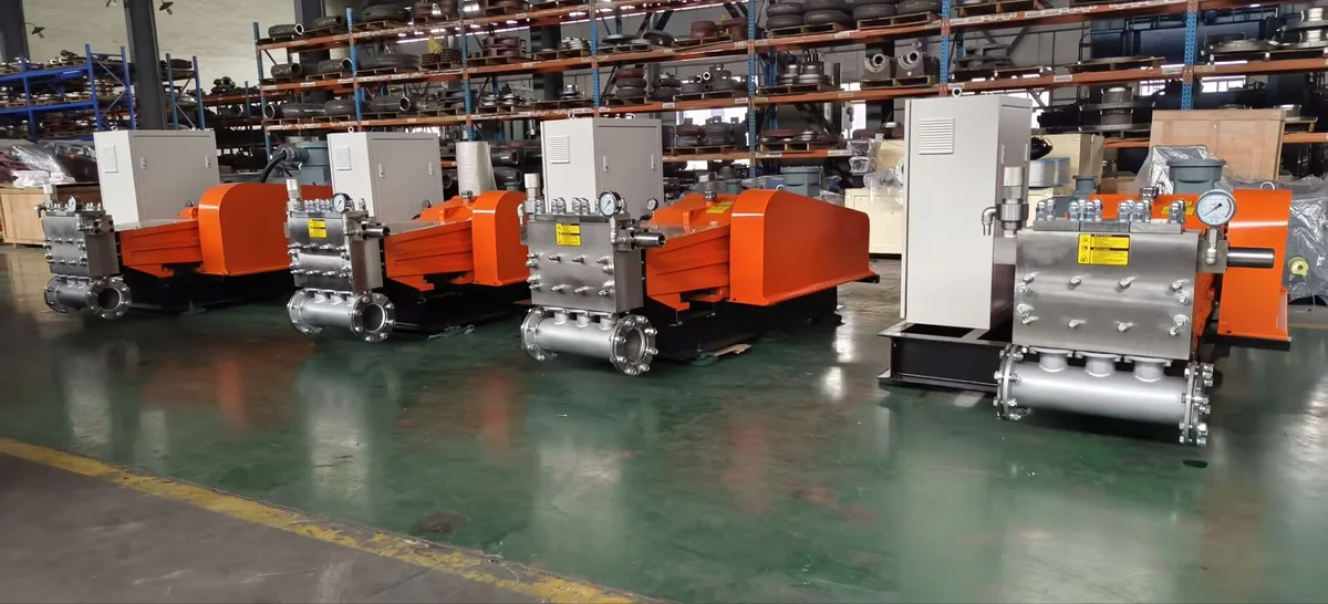 A row of orange plunger pumps and electric drives on common bases in the assembly workshop